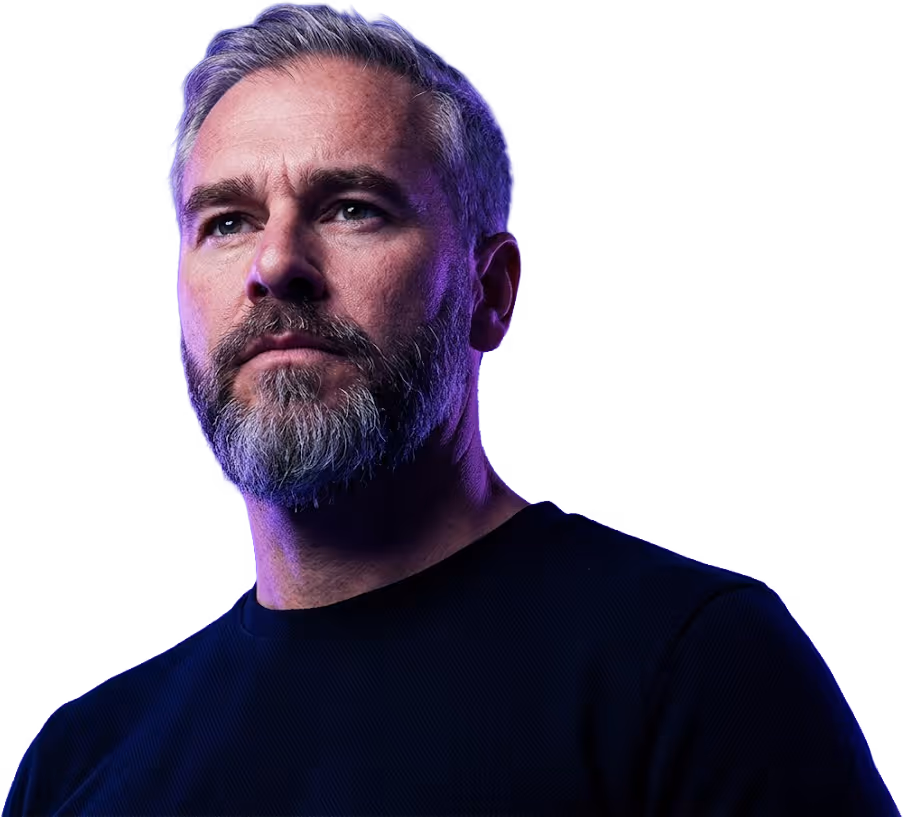 Middle-aged man with grey hair and beard wearing a black shirt against a purple background.